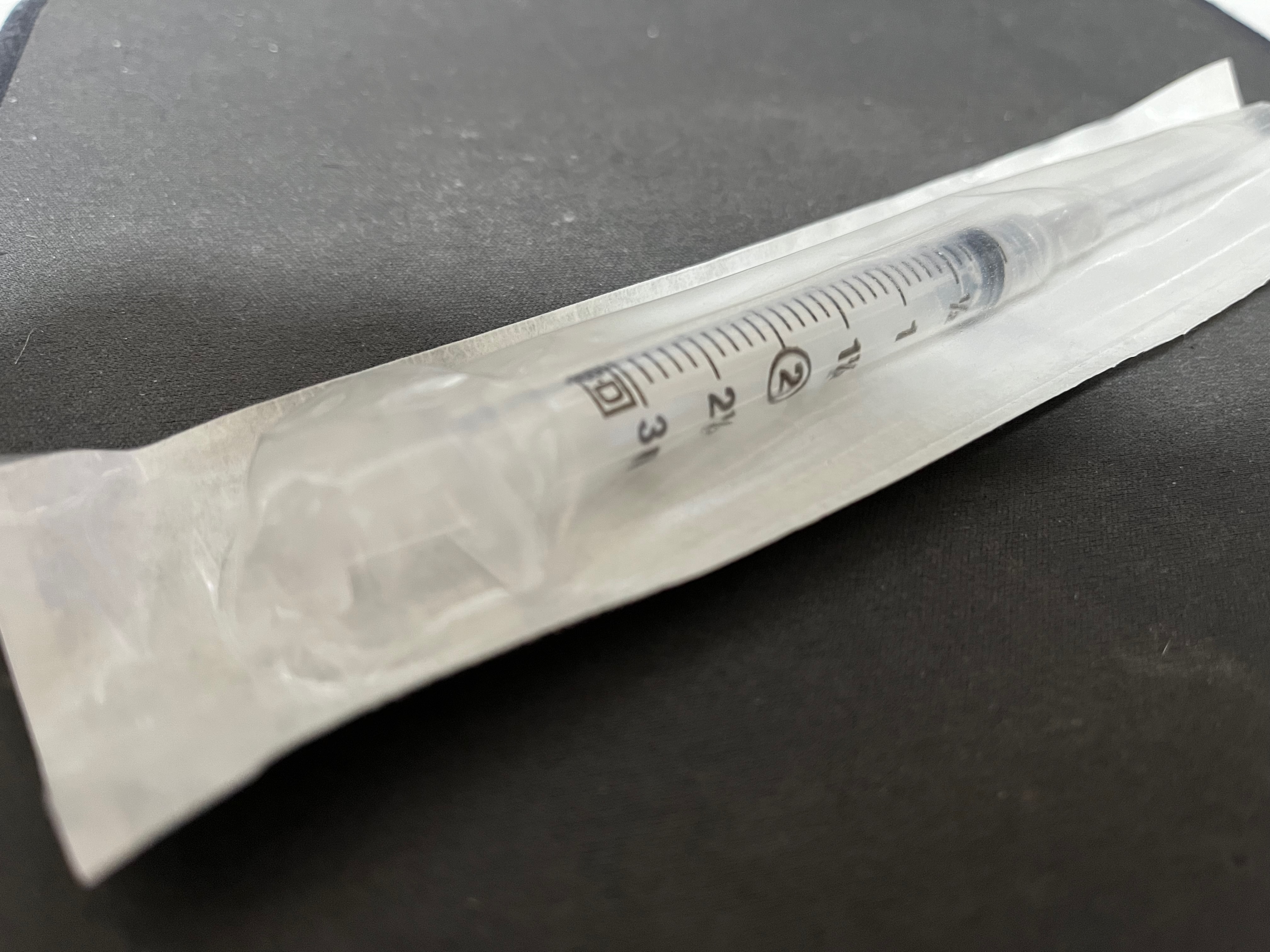 A photograph of a syringe for instramuscular injection with needle still in its wrapper.